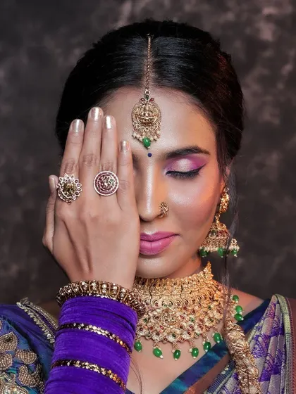 An artistic portrait of a model, her face partially covered by her hand. This pose draws attention to her dramatic eye makeup and the intricate rings on her fingers.
