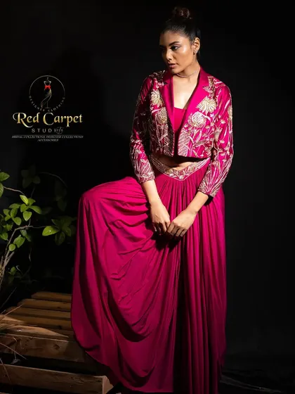 A full-length view of a model standing in a fuchsia pink Indo-Western outfit, featuring a draped skirt and an embroidered cropped jacket. This design is perfect for a sangeet or cocktail party.