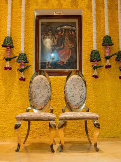 An indoor Haldi setup with a wall completely covered in yellow chrysanthemums. The traditional chairs and floral hangings complete the look, creating a vibrant and auspicious space.