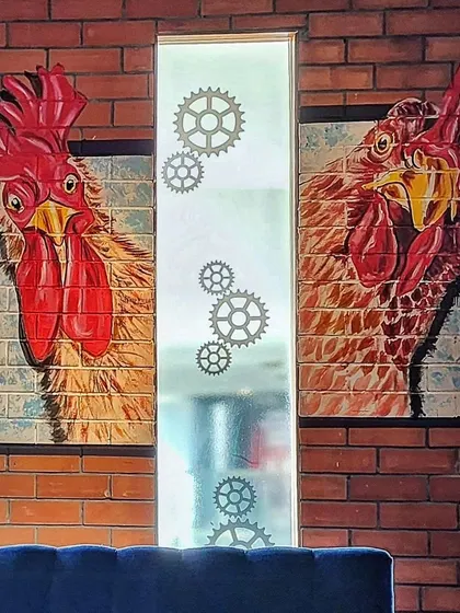 A close-up of two of the rooster portraits, each with its own personality, painted directly onto the brick-textured wall.
