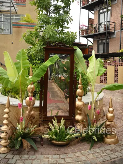 A photo booth setup with a personalized mirror, traditional brass props, and banana leaves, blending modern and traditional elements for a baby shower.