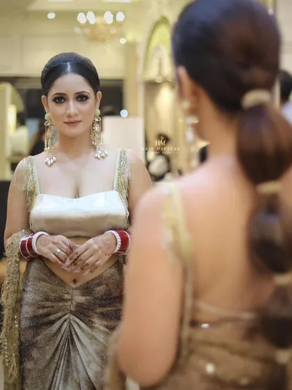 A modern and chic reception look. The client is looking in the mirror, showing off her smokey eyes and a trendy bubble ponytail.