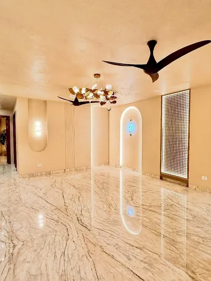 This expansive living room is designed for a feeling of openness and calm. The lime-washed walls, polished marble floors, and minimalist lighting create a serene canvas. The sculptural ceiling fans and custom wall lights act as functional art pieces.