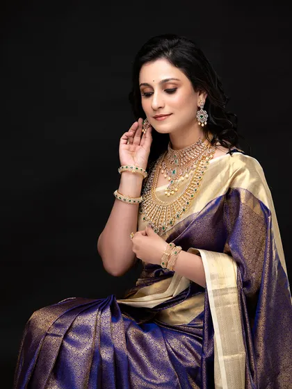A full-length seated portrait, showcasing the elegance of the saree and the understated, sophisticated makeup.