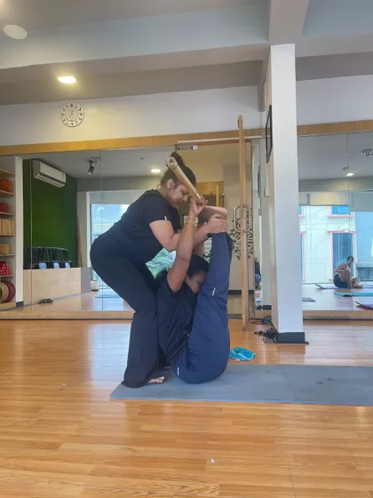 An instructor assists a student in a partner stretch using a stick, showcasing the community and supportive nature of our classes.