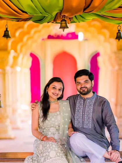 A happy couple poses on a decorated swing. Their light green and grey traditional outfits create a soft and elegant color palette.