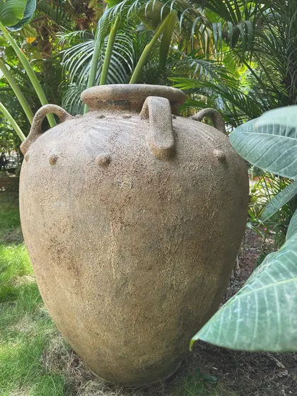 The 'Gentong' planter, nestled in a garden. Its large size and antique finish make it a perfect statement piece for outdoor spaces.