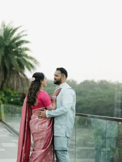 A wide shot of the couple against a scenic background, showcasing the bride's elegant saree and hairstyle.