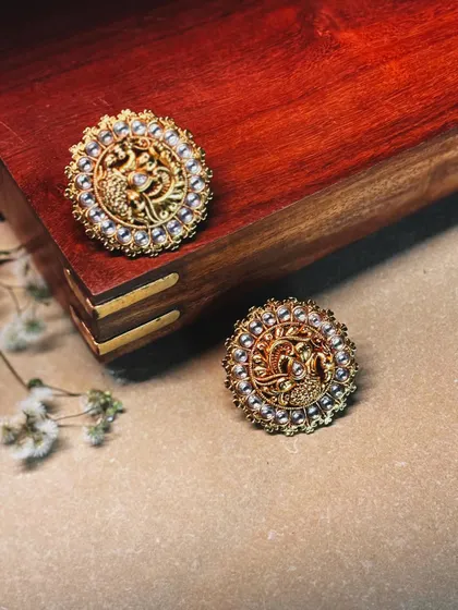 Intricate peacock motifs are carved into these gold-toned studs, surrounded by a halo of delicate pearls.