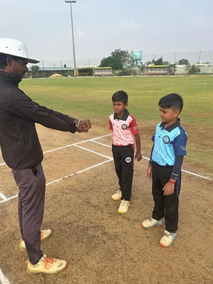 An umpire conducts the coin toss with the two young captains before their RSCA League match, instilling principles of fair play.