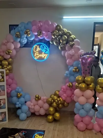 An "Oh Baby" gender reveal party with a balloon ring in pink, blue, and gold, and matching balloon pillars.