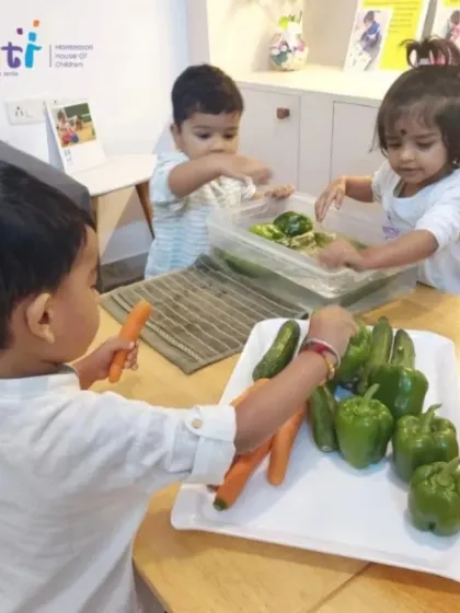 Three toddlers are fully engaged in washing cucumbers and carrots. These simple, purposeful tasks help develop their concentration and fine motor skills.