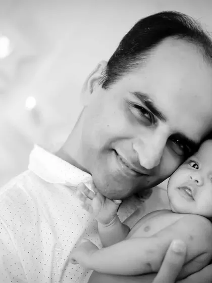 A proud father holds his newborn, a gentle smile on his face. A classic black and white portrait from an in-home session.