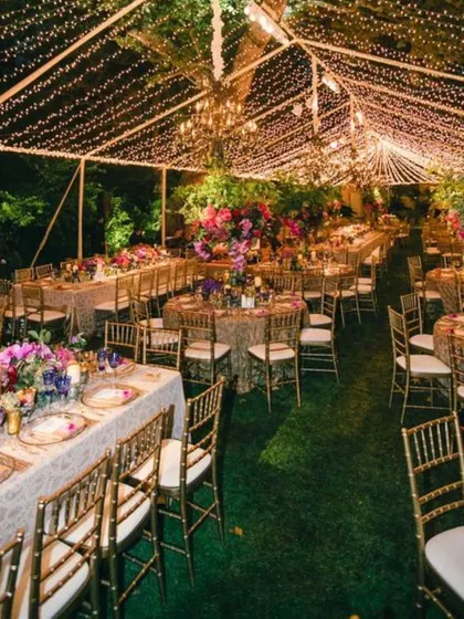 A breathtaking outdoor evening reception under a canopy of fairy lights. The long tables are beautifully set, creating a magical and grand setting for a large celebration.