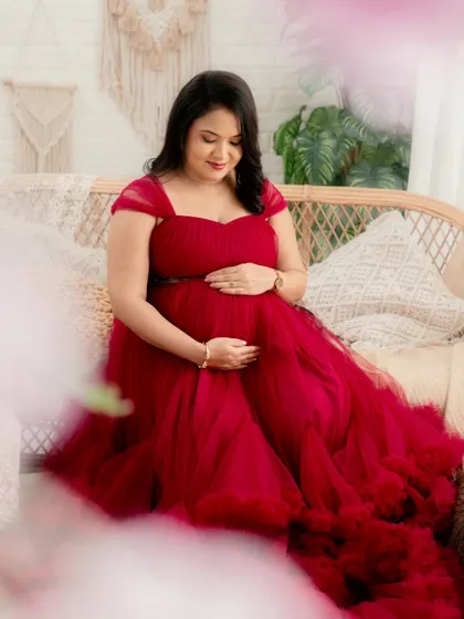 A quiet moment of connection. This portrait captures the mom-to-be looking down at her bump, framed by soft, dreamy elements in a beautiful red gown.
