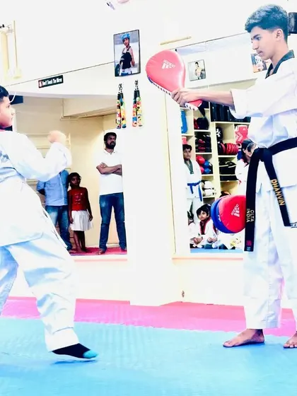 A young student practices his punch on a target held by a senior.