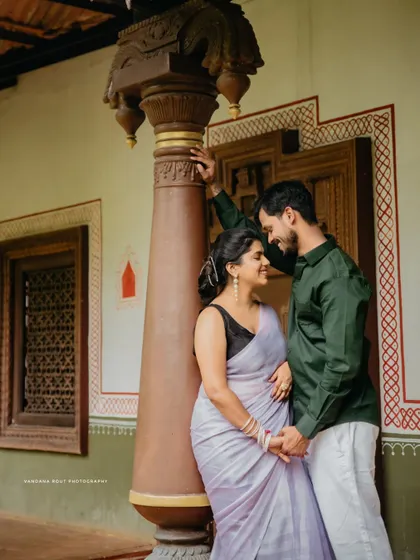 A classic portrait of a couple posing against the pillar of a traditional house, showcasing their connection and the beauty of their ethnic attire.