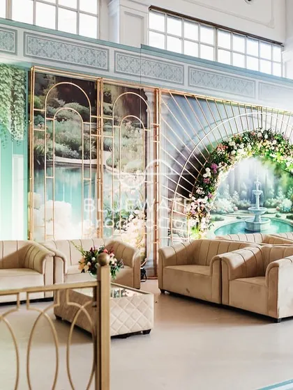 A cozy lounge nook with beige sofas set against a backdrop of artistic panels depicting a serene fountain scene.
