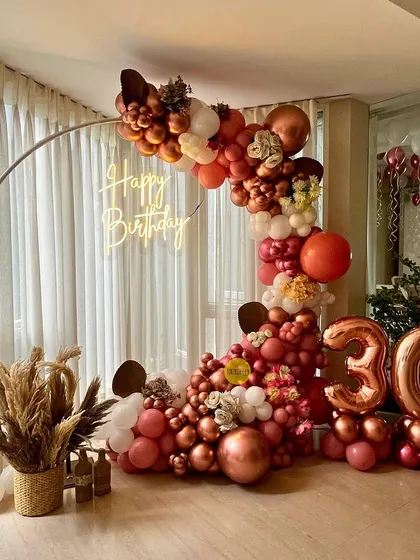 A trendy and rustic setup for a 30th birthday. The circular frame is decorated with a cascade of balloons in earthy tones and rose gold, complemented by pampas grass for a touch of boho elegance.