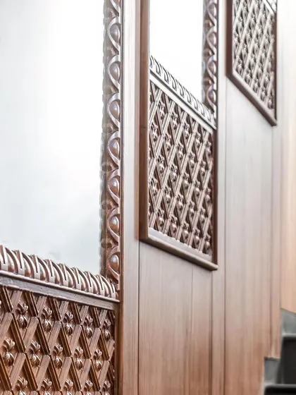 The staircase wall is a feature in itself, with teak paneling, embedded mirrors, and intricate wood-carved trims that exude regal splendor.