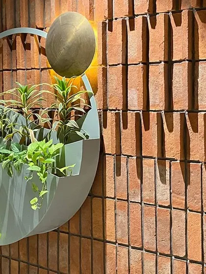 The play of light and shadow on the textured brick wall enhances the wall art. The brass "sun" catches the light, while the planter's curves, meant to depict the flow of wind, create a sense of gentle movement.
