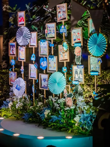 A photo display from a "Boss Baby" themed party. Pictures are arranged on a lit-up stage, surrounded by blue and white paper fans and other thematic elements.