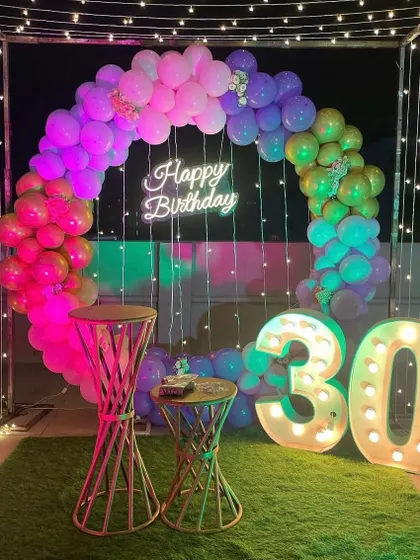 A close-up of the 30th birthday terrace decoration, showing the vibrant balloon ring and the large light-up marquee numbers against the night sky.