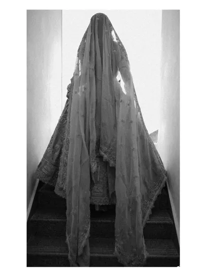 An artistic, mysterious shot of the bride veiled, descending a staircase. The black and white photo creates a dramatic and timeless image, focusing on the silhouette and the flow of the veil.
