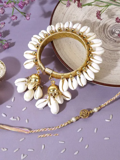A festive flatlay for Raksha Bandhan, featuring a beautiful shell work Lumba rakhi set. The traditional elements like rice and kumkum create an authentic and celebratory mood.