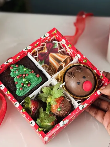 Our Christmas Special Treat Box is packed with festive goodies, including a Christmas tree brownie, chocolate covered strawberries, a jingle bells cookie, and a reindeer hot chocolate bomb.