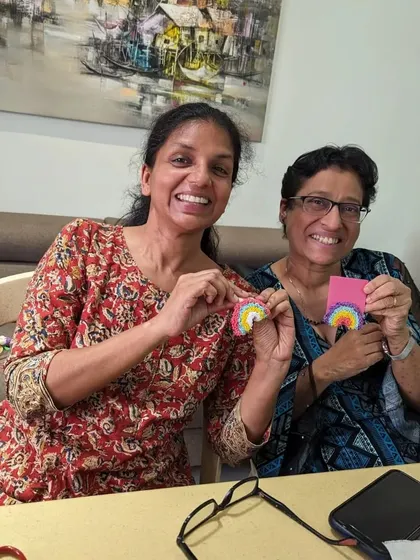 Two friends beaming with joy as they hold up their matching rainbow charms. Crafting is always more fun with a buddy.