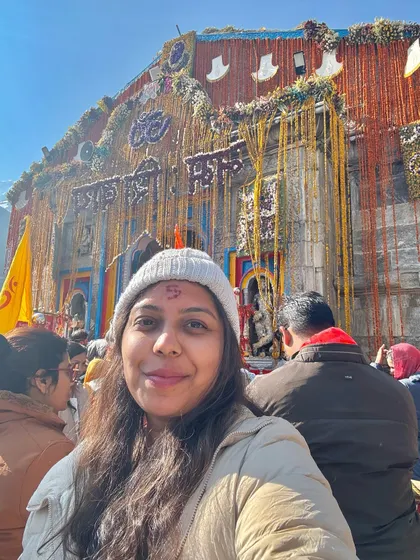 A happy traveler's selfie in front of the Kedarnath temple. Her smile and the tilak on her forehead reflect the inner peace and joy of a successful pilgrimage.