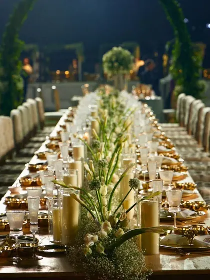A closer look at the intimate ambiance created by our long table designs. The combination of tall pillar candles and delicate floral arrangements provides a warm, inviting atmosphere for guests to connect.