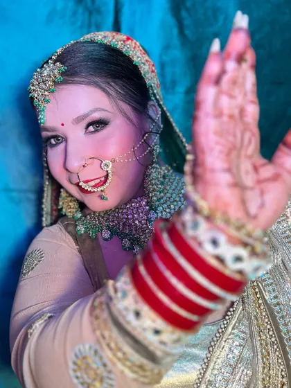 A playful and happy bride. This look features a stunning green and gold ensemble with a matching nath and maang tikka, perfect for a vibrant wedding celebration.