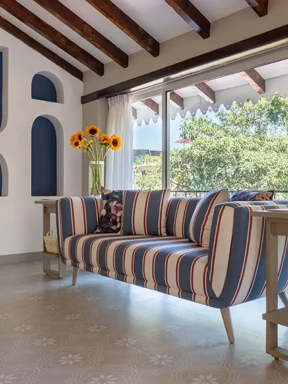 A cozy corner in the Goa villa, featuring a custom striped sofa that adds a playful touch. The exposed wooden beams and arched niches reflect the Portuguese heritage of the home.