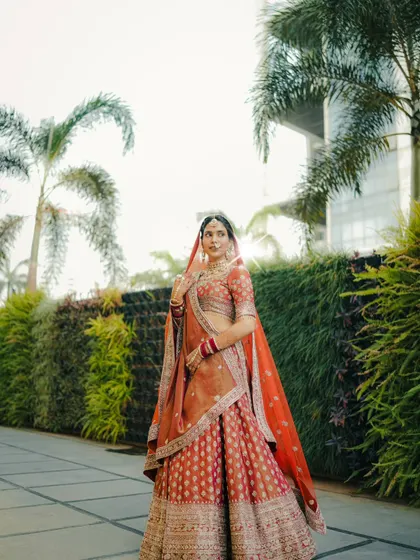 A full length bridal portrait set against a lush green backdrop. This shot showcases the bride's entire ensemble and her confident, regal posture.