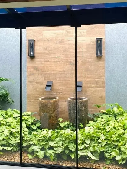 A closer look at the water feature in a glass-enclosed courtyard. The combination of wood-paneled walls, stone pots, and lush greenery creates a rich, textured look that is both modern and natural.