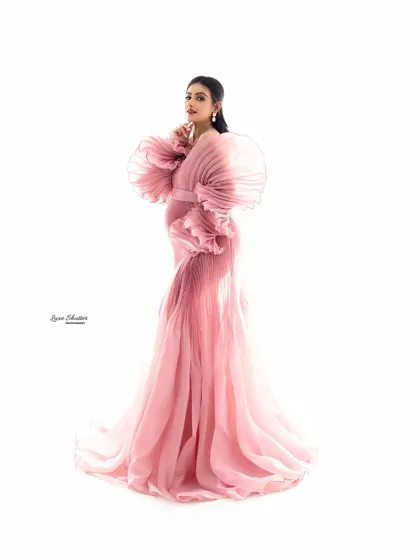 A pose that exudes confidence and grace. The dramatic ruffled sleeves of this pink gown frame the mother-to-be beautifully, creating a high-fashion, artistic look.