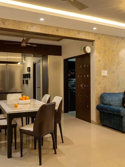 Here is a wide view of the renovated 'Blue Elegance' living and dining room. The space is unified by a soft, neutral palette, elegant floral wallpaper, and modern lighting, creating a sophisticated communal area.