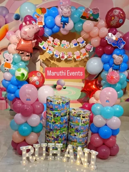 A full view of a Peppa Pig party setup, with a balloon arch, themed plinths, and light-up letters for the birthday girl's name.
