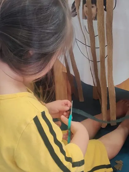This child shows great control as she snips away at the paper hair. Mastering the use of tools like scissors is a huge confidence booster for young learners.