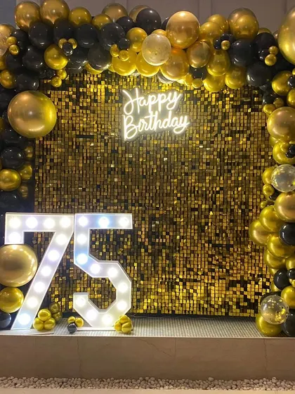Another view of the 75th birthday setup, showing the full scale of the gold shimmer wall and the black and gold balloon frame.