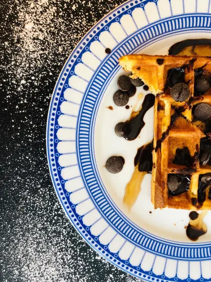 A classic chocolate chip waffle, artfully captured from above. The dusting of powdered sugar and drizzled chocolate sauce adds texture and a sense of indulgence to this dessert shot.