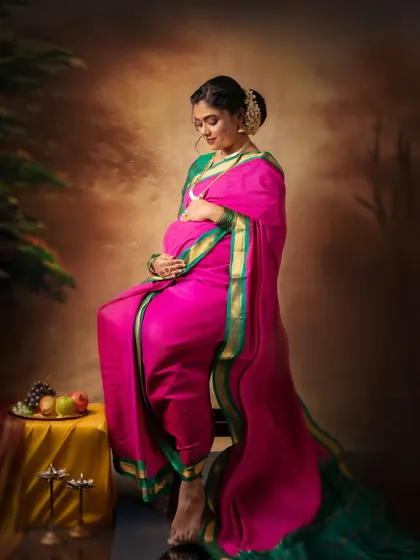 A full-length portrait showing the beautiful drape of the saree in a seated pose. This composition is carefully styled to feel both classic and comfortable, capturing the peaceful anticipation of motherhood.