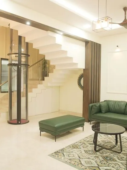 A full view of the villa's living room, showcasing the green leather sofas, open staircase, and minimalist wall paneling.