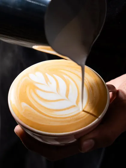 A barista creating latte art. This action shot showcases the skill and craft that goes into making a specialty coffee.