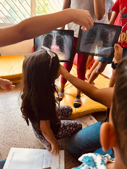 Two children hold up X-rays, comparing and discussing what they see. This kind of peer-to-peer learning is incredibly powerful and happens organically in our mixed-age environment.