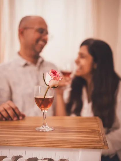 A beautifully composed shot with a wine glass and rose in the foreground and a smiling couple blurred in the background, symbolizing romance.