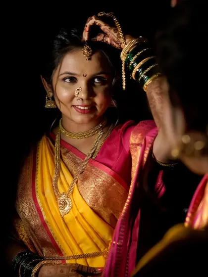 The bride adjusts her mundavalya, the traditional pearl strings worn on the forehead, in this classic mirror portrait.