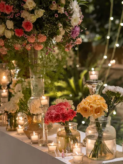 A console table decorated with an array of colorful flowers in clear glass jars, with dozens of tea lights scattered between them. This creates a beautiful, twinkling display of light and color.